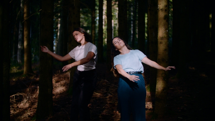 Deux femmes qui semblent danser dans une forêt, elles sont éclairées par le soleil