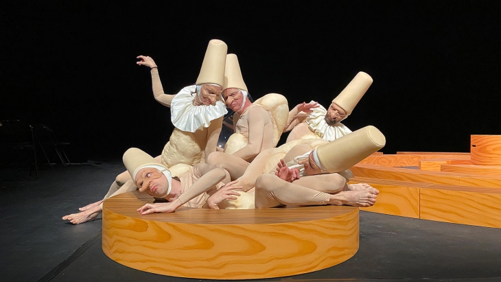 Des comédiens déguisés en polichinelle s'entassent et s'entre-mêlent sur une plateforme en bois 