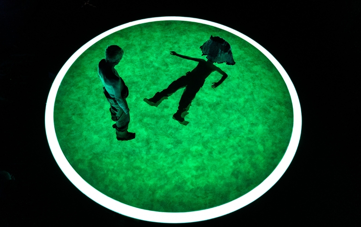 Au centre d'un cercle lumineux, un homme debout qui regarde un homme (costume futuriste), allongé