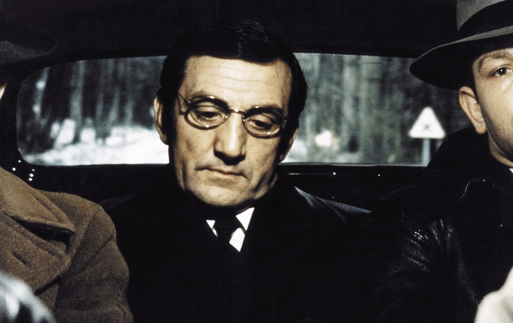 À l'intérieur d'une voiture, trois hommes. Le conducteur porte un chapeau. 