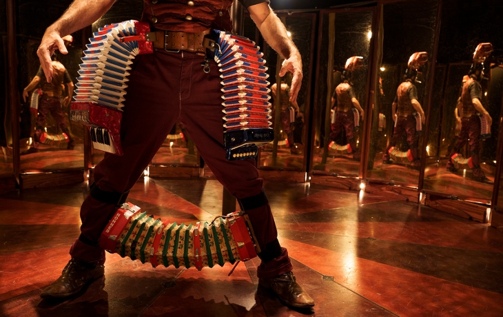 Sous un chapiteau, sur une petite scène circulaire encerclé de miroirs, se trouve au centre un interprète qui porte des accordéons à sa ceinture et entre ses chevilles.