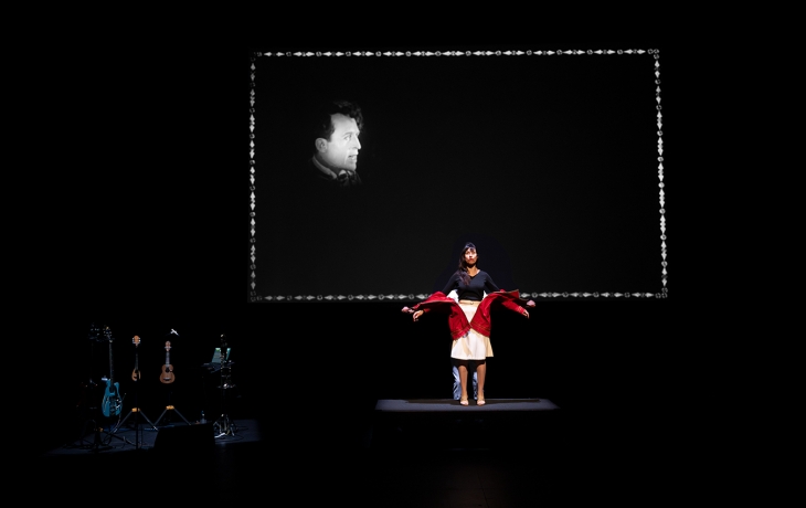  La comédienne est au centre avec un costume visiblement manipulé, et l’on distingue aussi un second interprète derrière elle. Le fond présente à nouveau une projection noir et blanc.