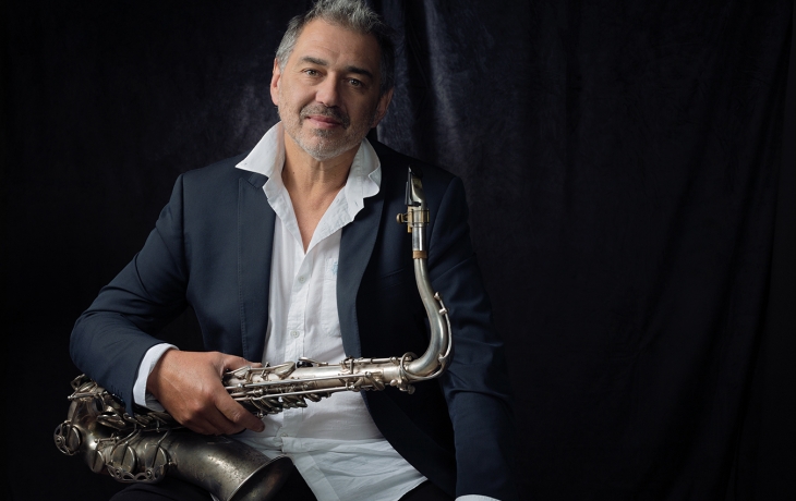 Guillaume Saint-James est en costume et pose pour la photo. Il regarde l'objectif et tient dans ses mains son saxophone. 