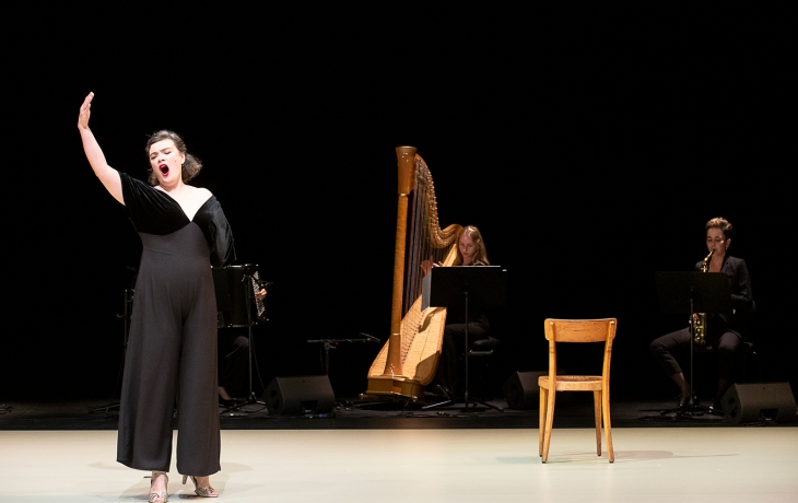Sur scène, les musiciennes sont à l'arrière plan. Au premier plan il ya RoseMary qui chante, le bras levé.