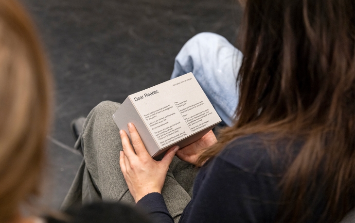 Plan serré au dessus des épaules d'une personne du public, sur un livret tenu dans ses mains
