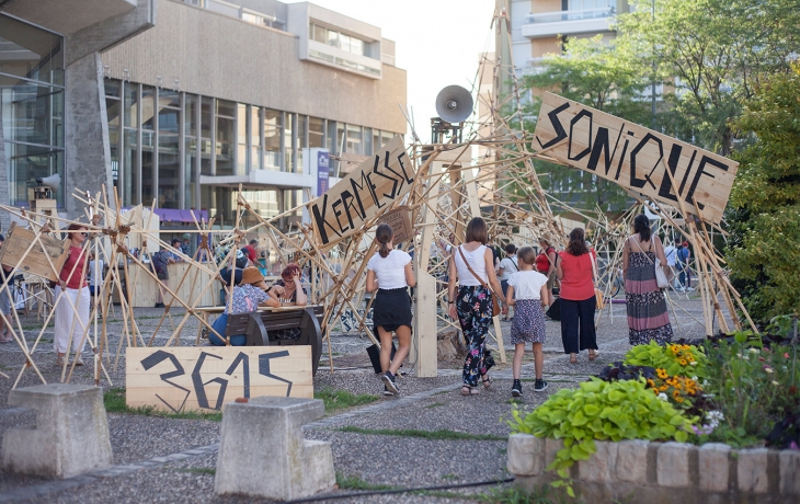 Prise de vue extérieure de la Kermesse sonique. Tout est fait en bois, en panneaux et tiges en bois. Des enfants jouent dans l'installation.