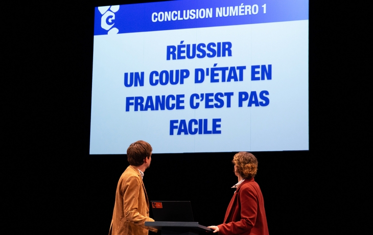 Les deux personnes regardent un écran géant qui affiche en bleu : "Réussir un coup d'État en France c’est pas facile". L’affirmation, provocante, semble être le point de conclusion d’un exposé critique ou satirique.