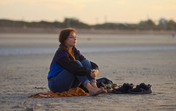 Sur une plage déserte, une femme est assise et regarde le couché de soleil.