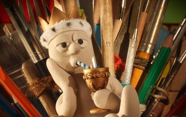 Coiffé d'une couronne dorée, Morph est sur un trône en crayons de papier et sirote une boisson dans une coupe en or.