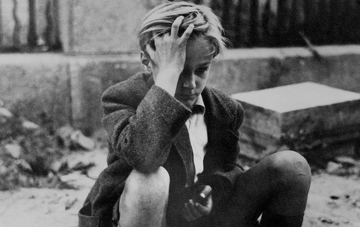 Photo en noir et blanc. Gros plan sur le jeune garçon qui est assis et semble inquiet. Il regarde dans le vide, la main sur sa tête, les cheveux ébouriffé.