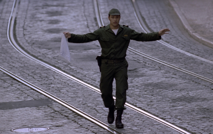 Au milieu de la rue qui est déserte, un soldat marche les bras en l'air, en tenant un mouchoir blanc, comme symbol de paix.