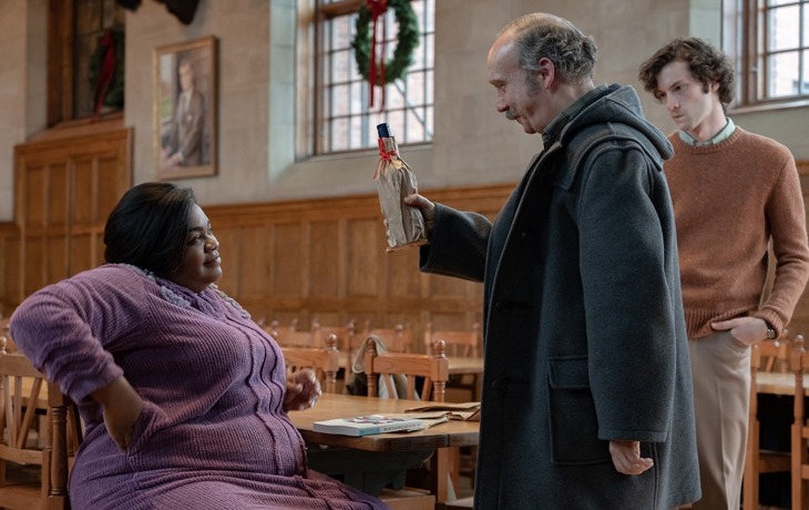 3 protagonistes dans une salle, l'homme offre une bouteille à la femme