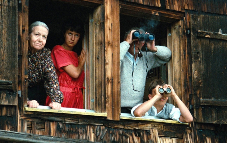 La famille regarde par la fenêtre. Deux d'entre eux ont des jumelles.
