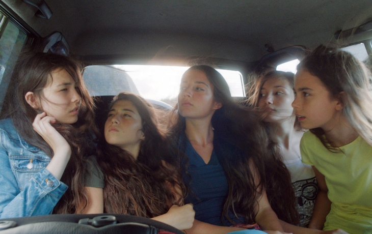 cinq soeurs sont assises à l'arrière d'un véhicule, le vent d'une fenêtre ouverte fait voler leurs cheveux 