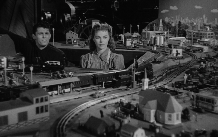 Un homme et une femme regardent attentivement la maquette d'un train qui prend toute la place.