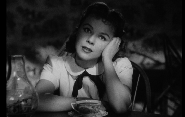 Dans l'obscurité, une femme regarde face à elle l'air songeuse.