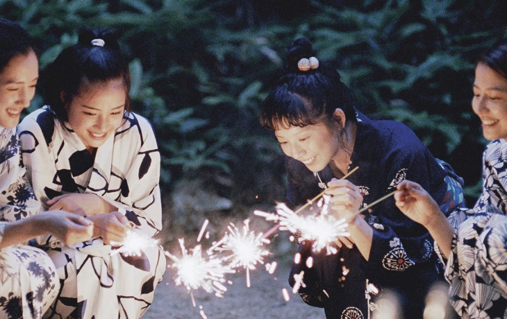 Les quatre soeurs sont en habits traditionnels et accroupis au sol. Elles tiennent des bâtons qui font des étincelles.