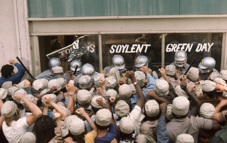 Une foule de personne dans le besoin est en colère devant une devanture protégée par des forces de l'ordre