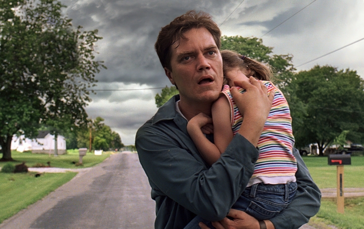 Au milieu d'une route, un homme tient sa petite fille dans ses bras pour la protéger d'une tempete qui arrive.