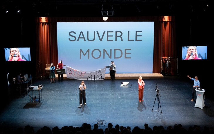 6 acteurs et actrices sont sur scène, un grand écran affichant "sauver le monde" derrière eux. Ils animent un débat 