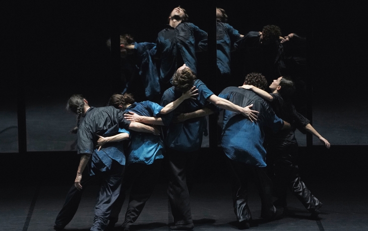 5 danseurs et danseuses, dos au public, se tiennent par les bras, leur image se reflétant dans un miroir 