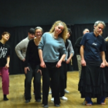 Plusieurs personnes se tiennent debout, en effectuant des positions et mouvements similaires, les épaules relevées et la tête penchée sur la droite.