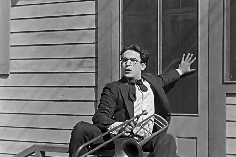 Homme devant une porte, tenant son trombonne. Image en noir et blanc