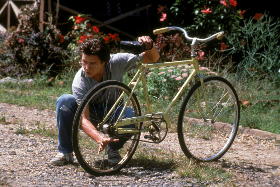 Un homme répare son vélo sur un chemin. Il regarde au loin 