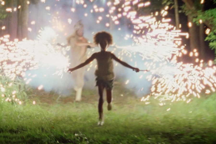Jeune fille en train de courir, suivie par un homme tenant des feux d'artifices