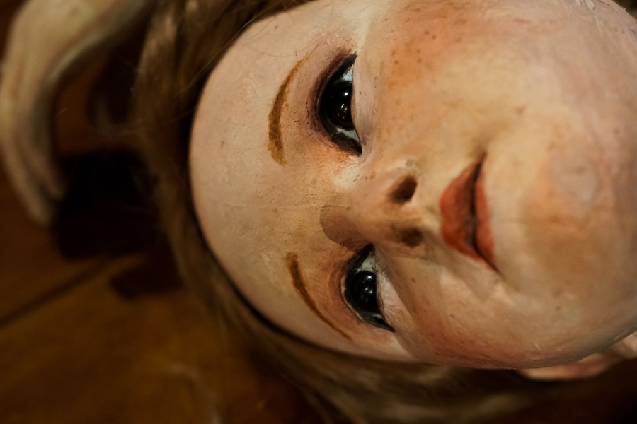 Photo en gros plan sur le visage d'une poupée qui est allongée sur un parquet.