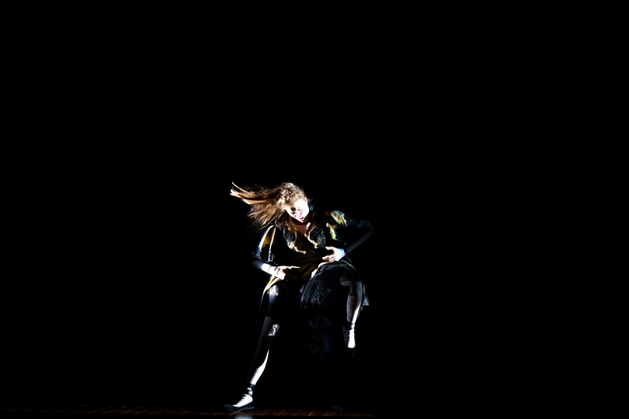 Photo très sombre où on voit uniquement une femme danser au centre, tout son corps est en mouvement