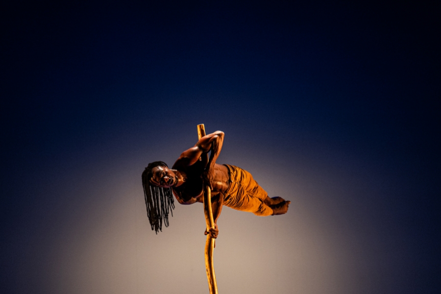 Un circassien tient en équilibre tout en haut d'un grand bâton avec ses bras