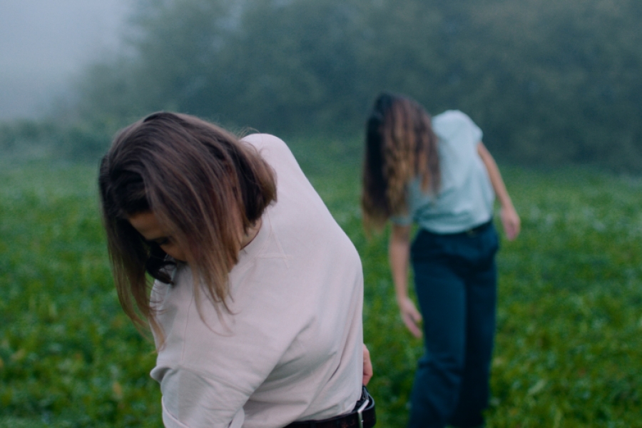 Deux femmes dans un champs brumeux. Une au premier plan, l'autre au second plan. On ne voit pas leurs visages, car elles ont la tête penchée vers le sol et leurs cheveux tombent sur le visage.