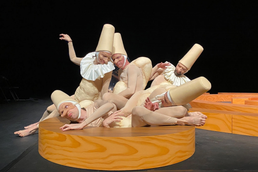 Des comédiens déguisés en polichinelle s'entassent et s'entre-mêlent sur une plateforme en bois 