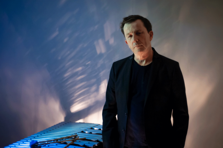 Un homme en veste noire, Franck Tortiller, debout à côté d'un vibraphone éclairé de manière artistique avec des reflets bleutés sur le mur derrière lui