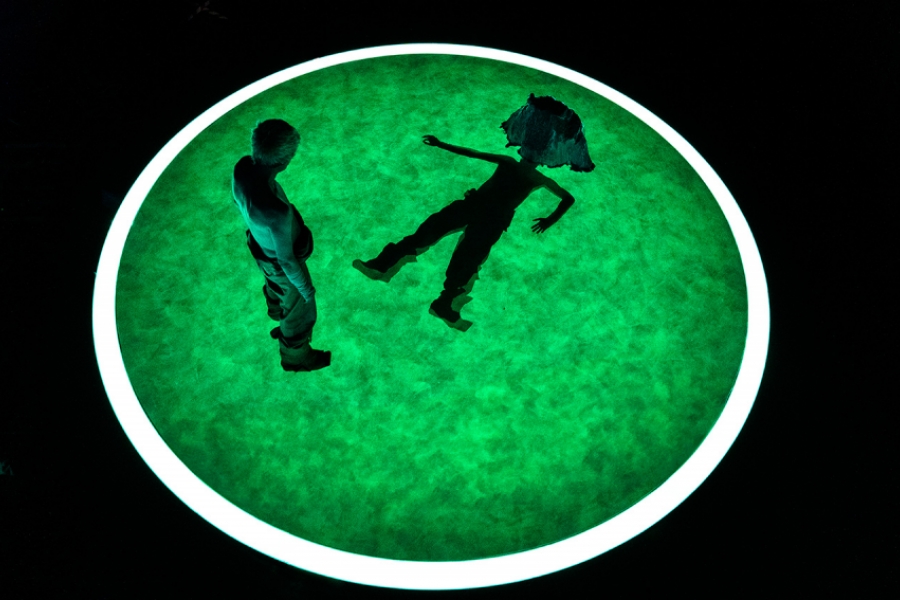 Au centre d'un cercle lumineux, un homme debout qui regarde un homme (costume futuriste), allongé