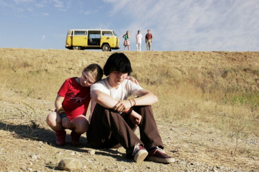 En premier-plan, jeune fille soutenant son frère triste, en arrière plan le reste de la famille et le van, dans un décor désertique