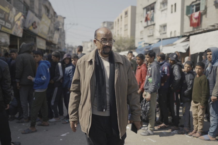 Un homme (enseignant) devant une queue de jeunes hommes qui attendent devant des batiments