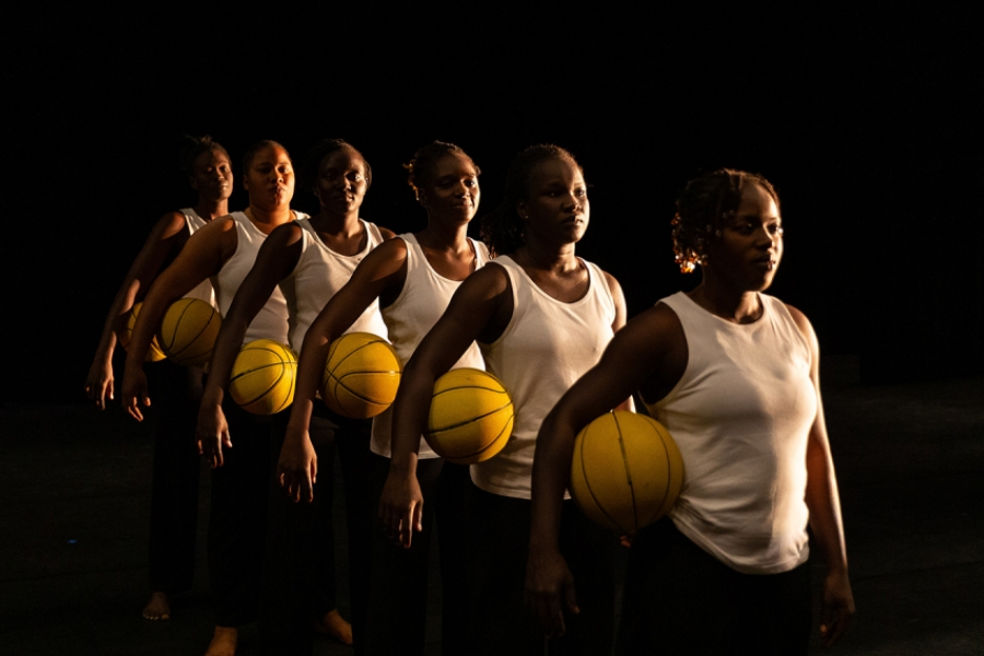 Les six interprètes sont e ligne les une derrière les autres, en se tenant droite avec chacune un ballon de basket jaune sous le bras. La photo est prise de trois quart, ce ui permet de voir toutes les interprètes.