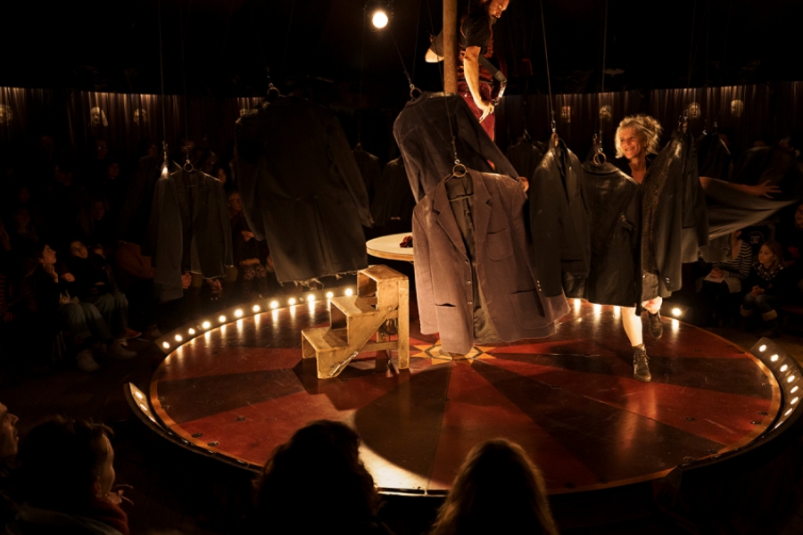 Sous un chapiteau, sur une petite scène circulaire, un grand porte-manteaux tournoi et fait voler dans les airs des vestes de costumes.