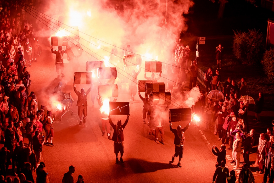 Dans la rue, le public laisse place a une déambulation chaotique. Les interprètes portent au-dessus de leurs têtes des tonneaux. Il y a beaucoup de fumée avec des fumigènes, les couleurs sont d'un rouge vif.