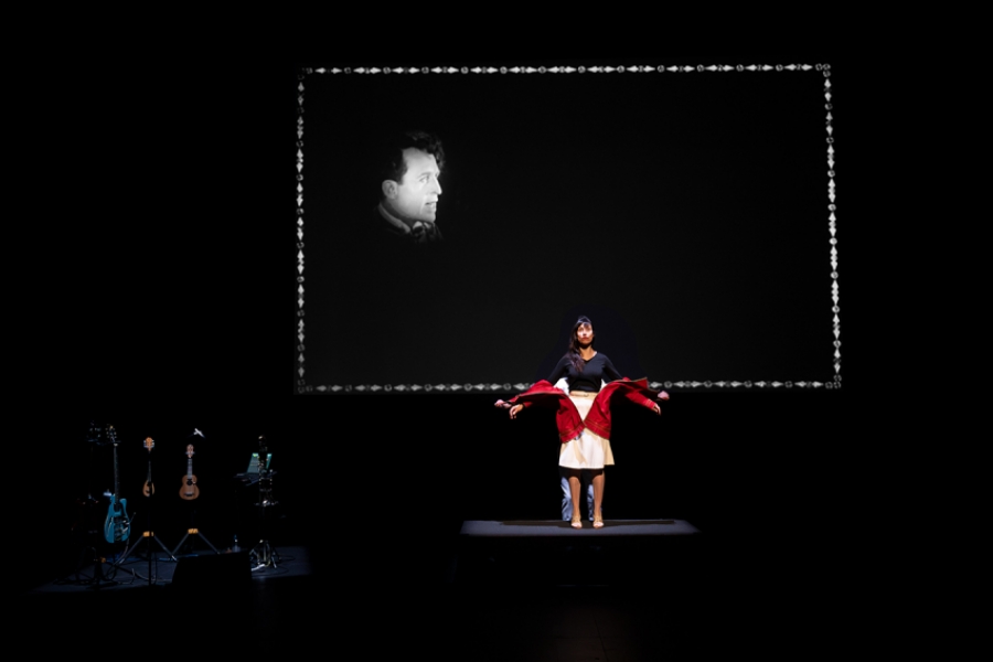  La comédienne est au centre avec un costume visiblement manipulé, et l’on distingue aussi un second interprète derrière elle. Le fond présente à nouveau une projection noir et blanc.