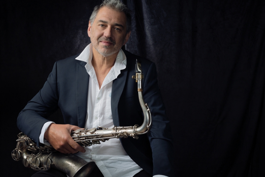 Guillaume Saint-James est en costume et pose pour la photo. Il regarde l'objectif et tient dans ses mains son saxophone. 