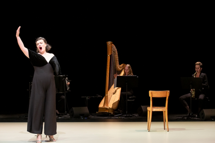 Sur scène, les musiciennes sont à l'arrière plan. Au premier plan il ya RoseMary qui chante, le bras levé.