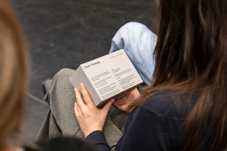 Plan serré au dessus des épaules d'une personne du public, sur un livret tenu dans ses mains