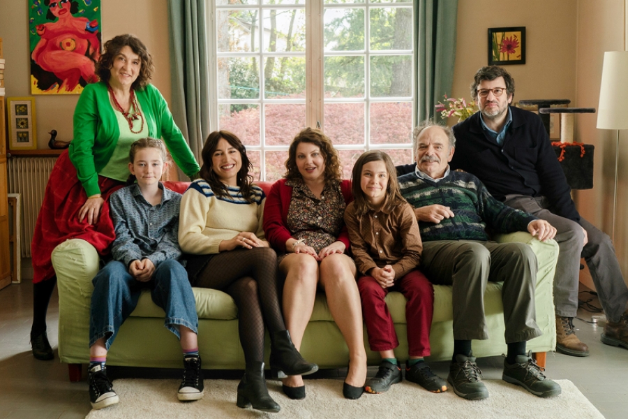 Photo de famille dans un salon, sur un canapé. Tout le monde regarde l'objectif.
