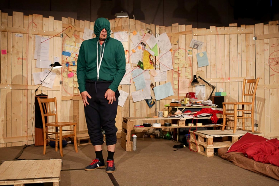 Au centre de sa scénographie circulaire et en bois, Thierry Combe est debout face au public, il porte un pull à capuche vert. La capuche sur sa tête, il ne voit plus rien.