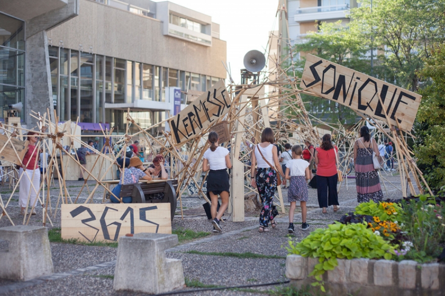 Prise de vue extérieure de la Kermesse sonique. Tout est fait en bois, en panneaux et tiges en bois. Des enfants jouent dans l'installation.