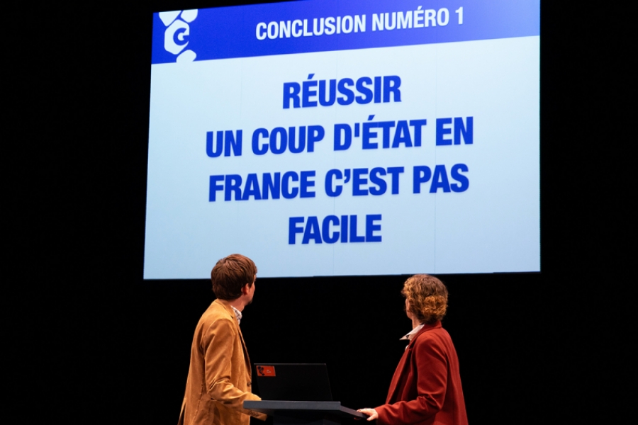 Les deux personnes regardent un écran géant qui affiche en bleu : "Réussir un coup d'État en France c’est pas facile". L’affirmation, provocante, semble être le point de conclusion d’un exposé critique ou satirique.