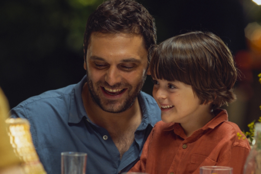 Un homme est à table et porte sur ses genoux un petit garçon, ils ont l'air heureux.